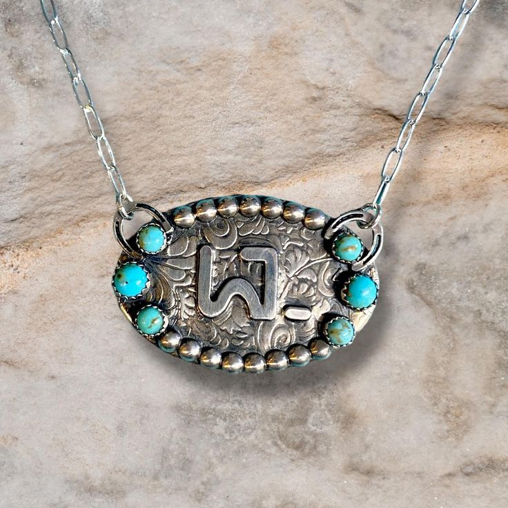 Show your cowgirl spirit in style with this Custom Oval Brand Necklace! This stylish accessory features an oval brand pendant with a stunning turquoise and textured background. Giddy up to the most eye-catching necklace in town! Features: This custom Oval Brand Necklace is made with solid sterling silver Kingman turquoise stones of multiple sizes. It measures 1.5 in. x 1 in. and makes a timeless addition to any jewelry collection. See Options for more details. Western Jewelry Cheekys Boutique, Western Turquoise Necklace, Luxury Southwestern Oval Necklace, Luxury Turquoise Necklace With Oval Pendant, Western Oval Engraved Jewelry, Western Style Oval Engraved Jewelry, Artisan Oval Turquoise Necklace Nickel Free, Silver Smithing Jewelry, Western Jewelry Necklace