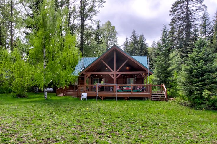 a log cabin sits in the middle of a field with trees and grass around it