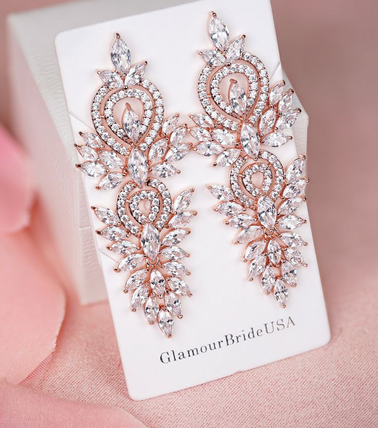 two pairs of diamond - bridal usa earrings are on display in front of a pink rose