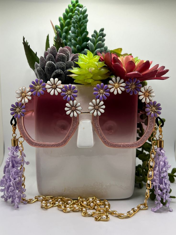 Daisies surround these polygon, square glittering sunglasses and are accompanied by an adjustable and removable eyewear chain and removable tassels. Featuring bold, fashion-forward designs, these glamorous sunglasses are perfect for making an entrance at any special occasion. Embellished and colorful, these fun and inspiring sunglasses will make sure you stand out in a crowd. Ideal for bachelorette parties, Vegas trips, weddings, birthdays, and more - Roaring Sunnies are the perfect accessory to Summer Party Glasses Chains, Multicolor Glasses Chains For Summer Parties, Multicolor Summer Party Glasses Chain, Summer Party Multicolor Glasses Chains, Gold Party Sunglasses With Adjustable Fit, Adjustable Multicolor Glasses Chains For Party, Purple Party Sunglasses, Purple Plastic Party Sunglasses, Trendy Adjustable Glasses Chains For Party