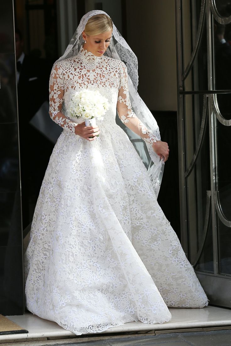 a woman in a white wedding dress and veil walking out of a doorway with her bouquet