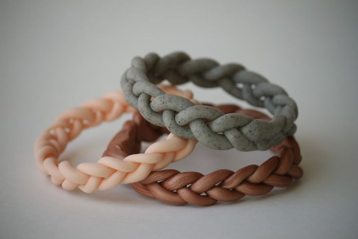 three different colored braid bracelets sitting on top of a white table next to each other