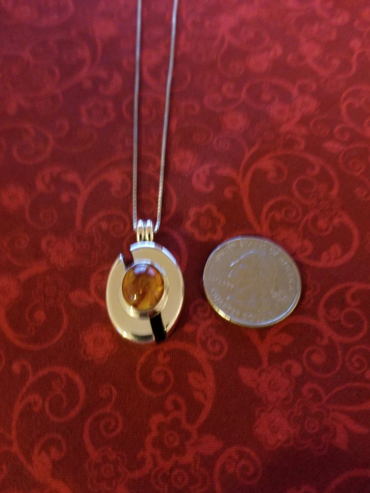 Silver modernistic pendant with amber colored stone. The pendant is oval, but it is split, the amber stone is at the center of the pendant. The pendant comes with a box chain necklace. Oval Baltic Amber Necklace, Modern Oval Amber Jewelry, Amber Oval Birthstone Necklace, Modern Amber Pendant Jewelry, Modern Amber Oval Jewelry, Amber Cabochon Oval Pendant Necklace, Formal Amber Necklace With Oval Pendant, Formal Amber Oval Pendant Necklace, Formal Amber Round Pendant Necklace