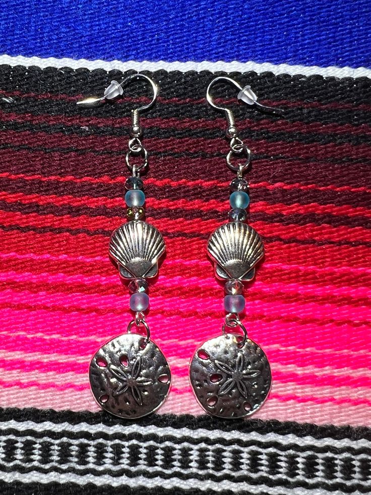 "These handmade sea theme earrings are adorned with silver plated metal shells along with blue semi-precious beads. The ear wire is metal and hypo allergenic.  The matching boot bracelets are available for sale as well. Earrings are 3 1/2\" long. Please see the photos for other earring styles. Price includes one pair of Sand Dollar Silver Shell Earrings with Crystals and Blue Beads. Not water-resistant. For pierced ears only." Adjustable Metal Earrings For Beach, Blue Metal Jewelry For Beach, Beach Beaded Metal Earrings, Metal Beaded Earrings For Beach, Handmade Metal Beaded Earrings For Beach, Nickel-free Silver Ocean-inspired Earrings, Nickel-free Silver Beaded Earrings For Beach, Nickel Free Silver Beaded Earrings For Beach, Silver Beaded Ocean-inspired Jewelry