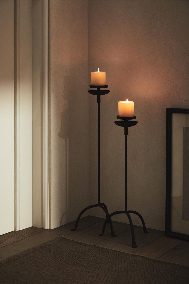 two lit candles sitting on top of a stand in front of a mirror and door