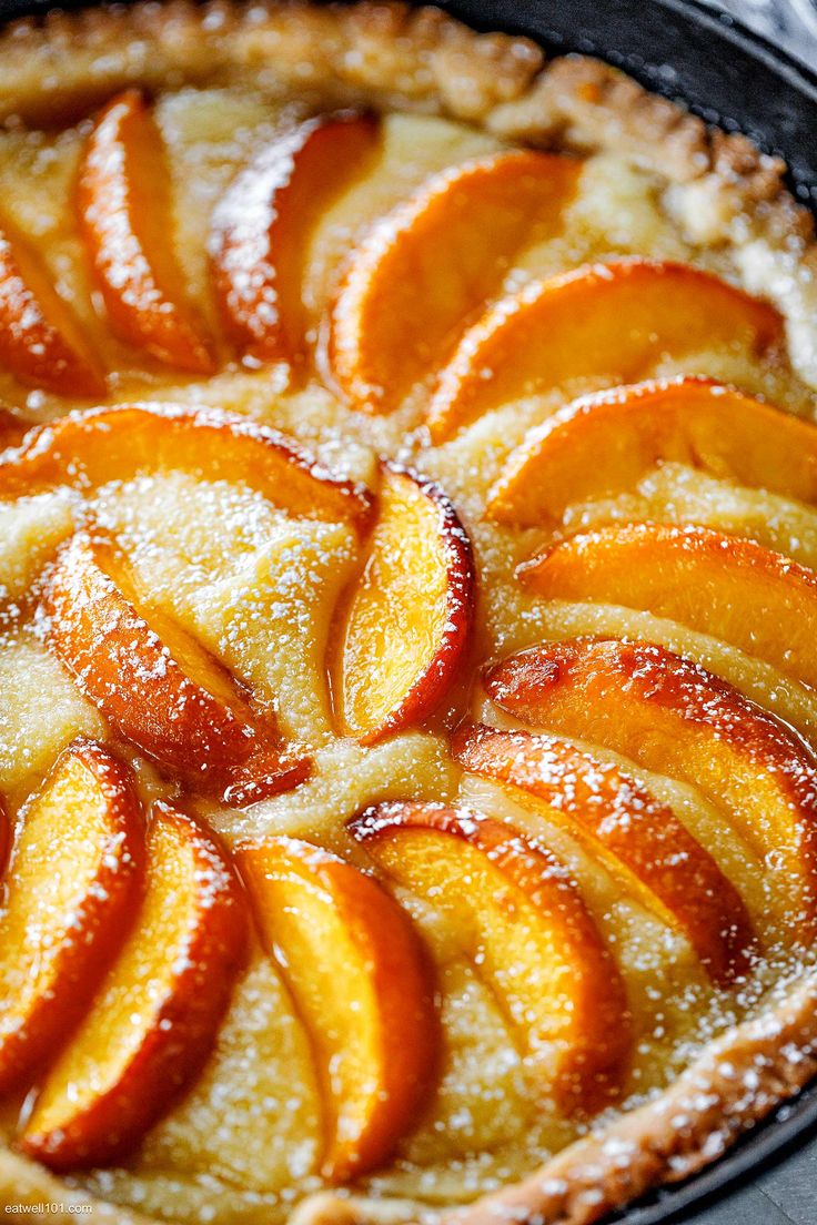 a pie topped with sliced peaches on top of a metal pan covered in powdered sugar