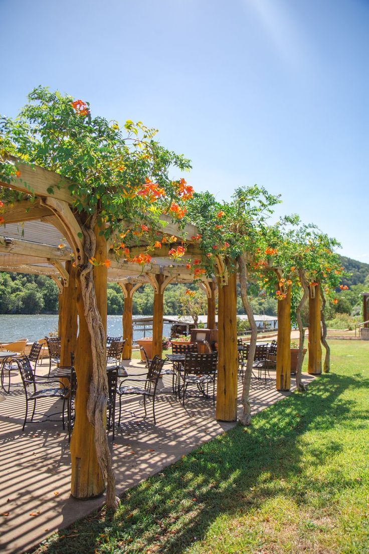 an outdoor dining area with tables, chairs and umbrellas on the grass next to water