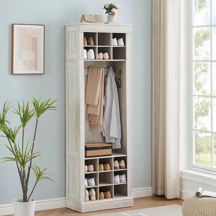 a white cabinet with shoes and blankets on it next to a potted plant in front of a window