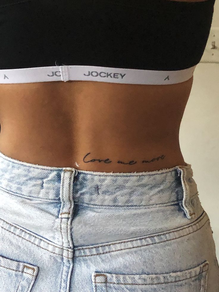 Back script tattoo reading, “love me more” Waist Back Tattoos For Women, One Worded Tattoos, Tattoo Ideas Waist For Women, Lower Back Writing Tattoo, Lower Back Quote Tattoo, Short Quote Tattoo Placement, Back Tattoo Phrase, Lower Back Small Tattoos, Lower Back Script Tattoos