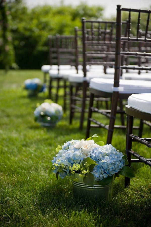 chairs lined up on the grass with flowers in buckets next to them for an outdoor ceremony