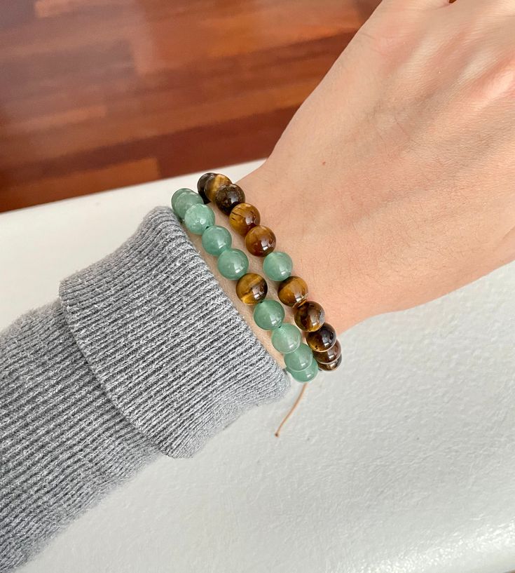 a woman's hand holding two bracelets with green and brown beads on them