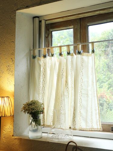 a vase with flowers sitting on a window sill in front of a curtained window