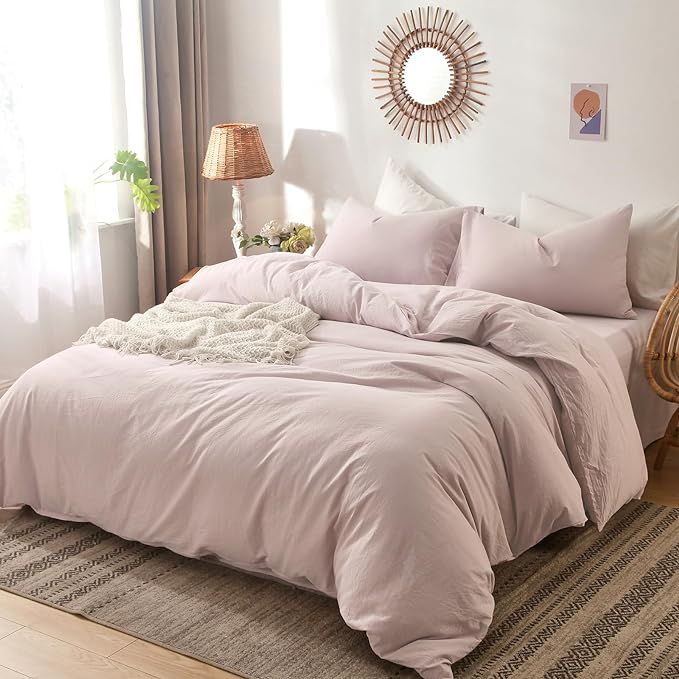 a bed with pink comforter and pillows in a room next to a lamp on a table