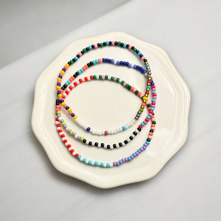 Add a touch of charm to your everyday look with our handcrafted Seed Bead Bracelets. Delicately made with tiny 2mm beads, they're the perfect lightweight accessory for layering up and creating your own style statement -- all without any bulk! Each bracelet is a little piece of art, featuring a delightful mix of colors and designs. And if you're looking for something just for you, we'd love to make it happen! Simply pick your favorite hues from our color chart, and we'll tailor it to your taste. These bracelets are strung on top-notch elastic bead cord for a snug, comfy fit. Plus, they come in a cute cotton pouch with the Georgia Goddess seal, ready to be the perfect gift or a special treat for yourself. *Note From Jess* I personally wear these bracelets for weeks at a time. Waterproof, swe 2mm Bead Bracelet Ideas, Everyday Multicolor Beaded Chain Bracelets, Friendship Bracelets With Spacer And Round Beads, Everyday Heishi Beaded Necklaces, Minimalist Beaded Chain Bracelets, White Beaded Chain Bracelets, Minimalist Beaded Necklace With Letter Beads, Minimalist Beaded Necklace With Round Letter Beads, Minimalist Multicolor Round Bead Friendship Bracelets