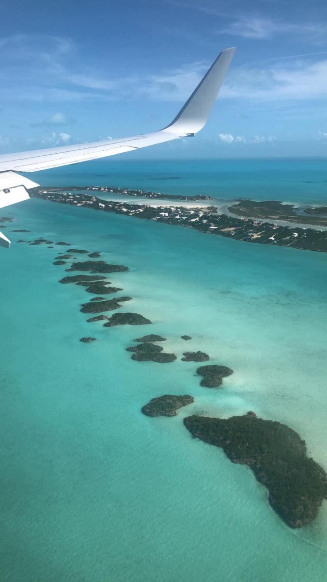 an airplane wing flying over the ocean with land and water in it's foreground