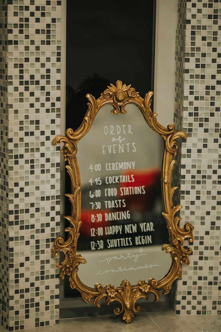 an ornate gold framed mirror sitting in front of a tiled wall with words on it