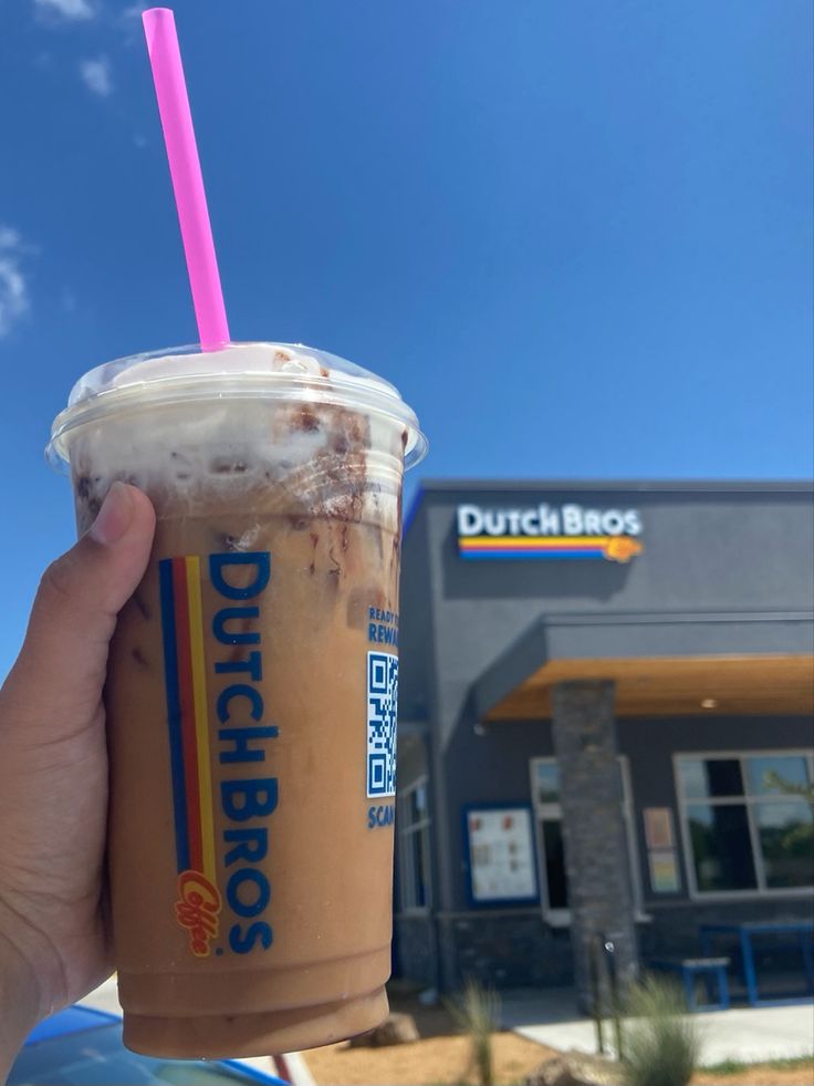 a person holding up a drink in front of a dunkin'donuts store