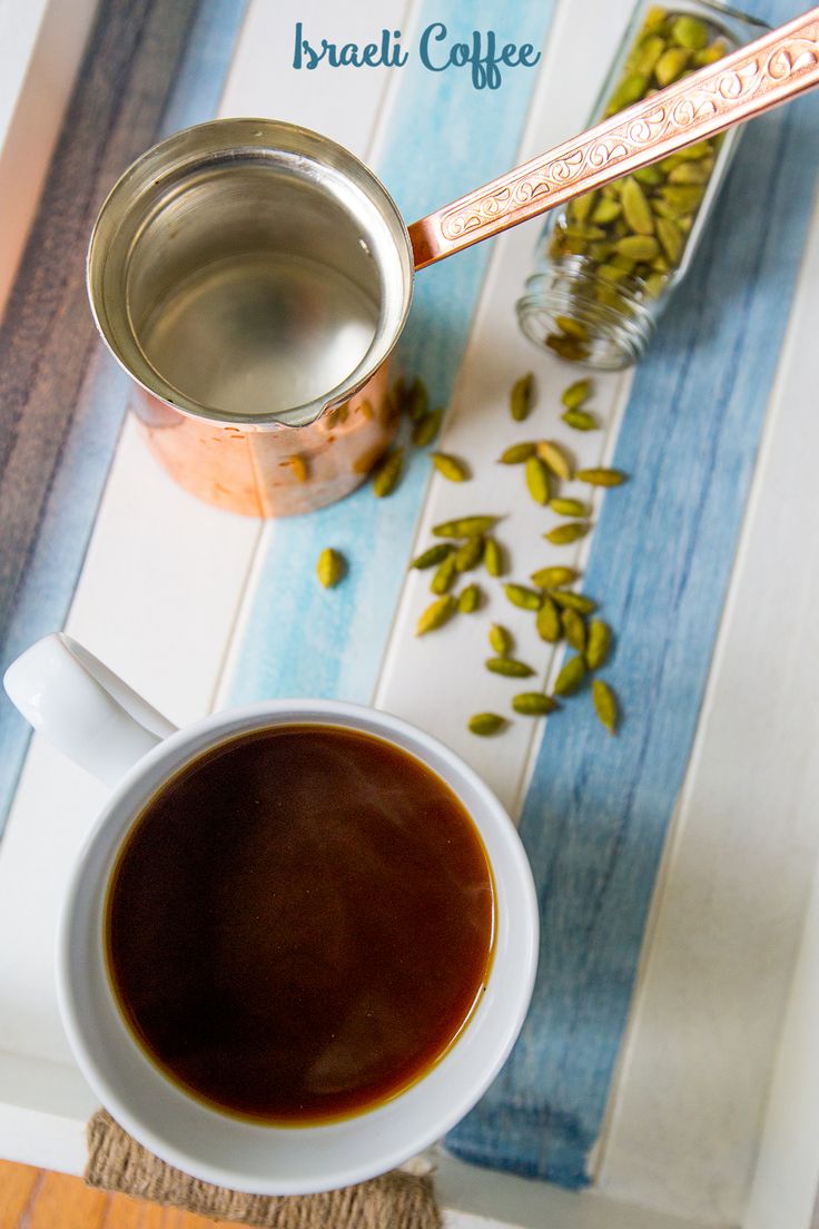 there is a cup of coffee next to a spoon and some seeds on the table