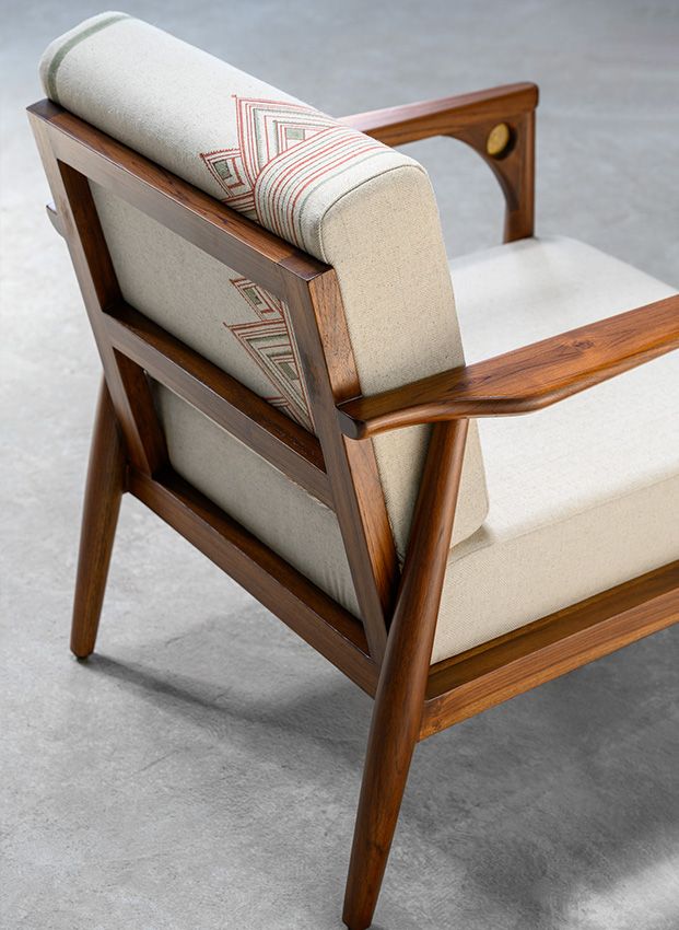 a chair with a wooden frame and arm rests on concrete flooring, in front of a gray background