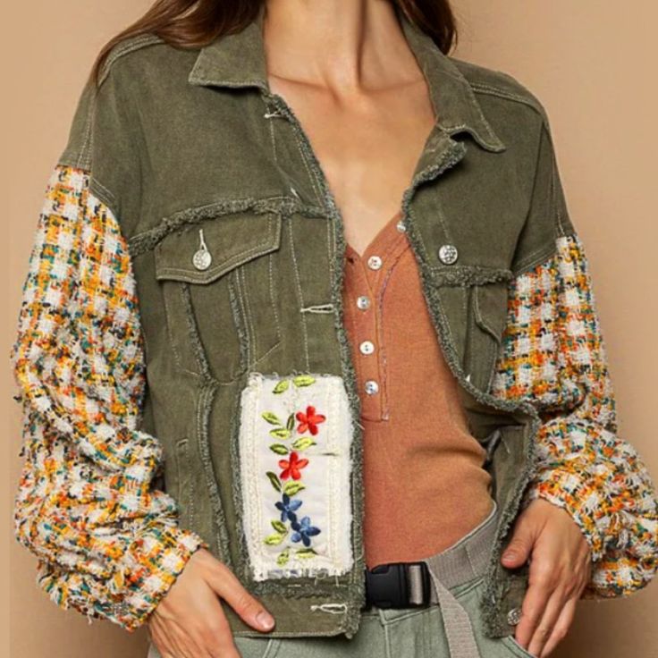 a woman wearing a jean jacket with flowers on the front and back pockets, standing in front of a beige wall