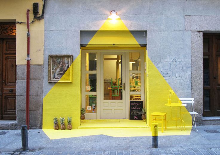 a yellow building with a white door and some chairs on the sidewalk in front of it