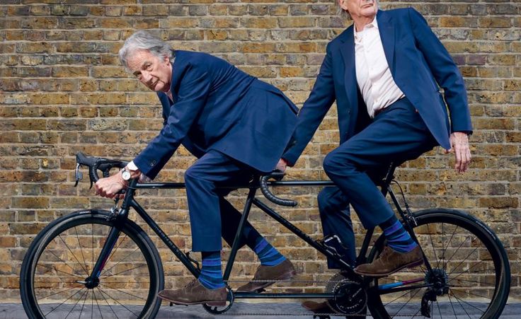 two older men in suits riding on the same bike