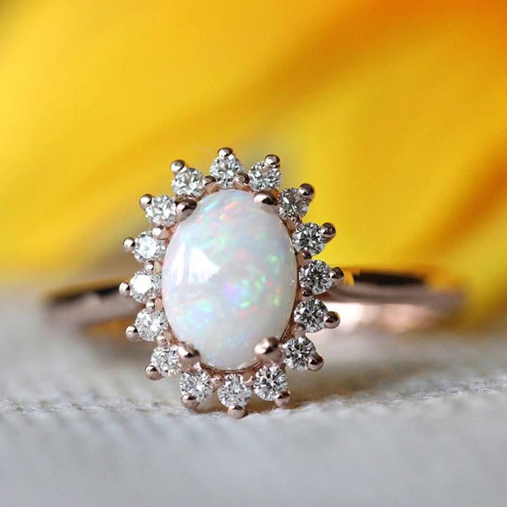 a white opal and diamond ring sitting on top of a yellow flower