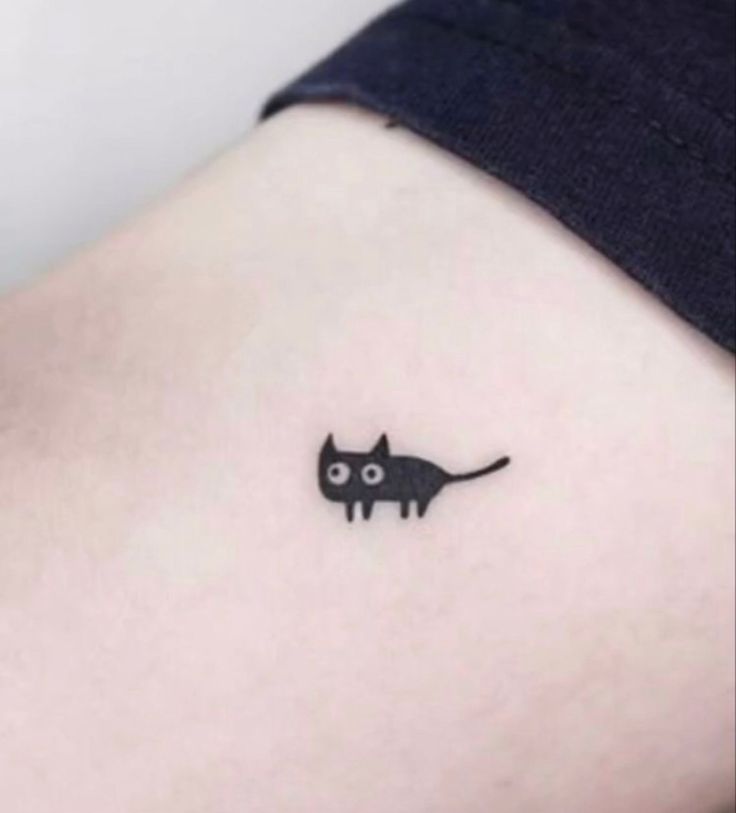 a small black cat tattoo on the side of a woman's right hip area