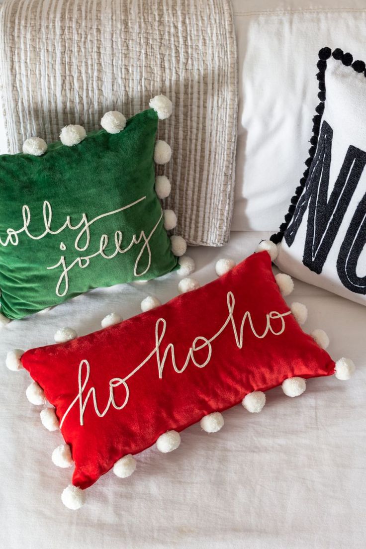 three christmas pillows on a bed with pom - poms and one pillow that says merry hoho