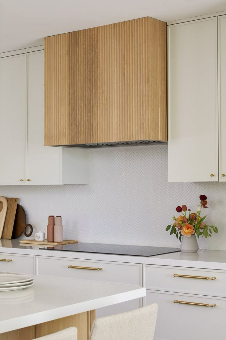 a kitchen with wooden cabinets and white counter tops, along with flowers in vases