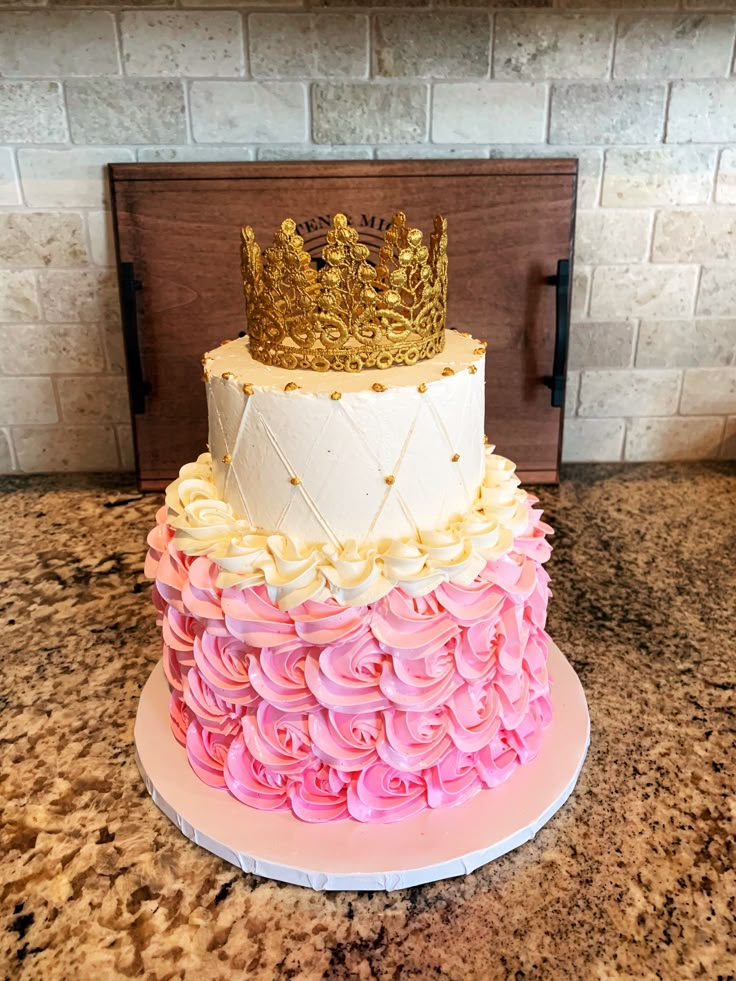 a three tiered cake decorated with pink and yellow icing, topped with a gold crown