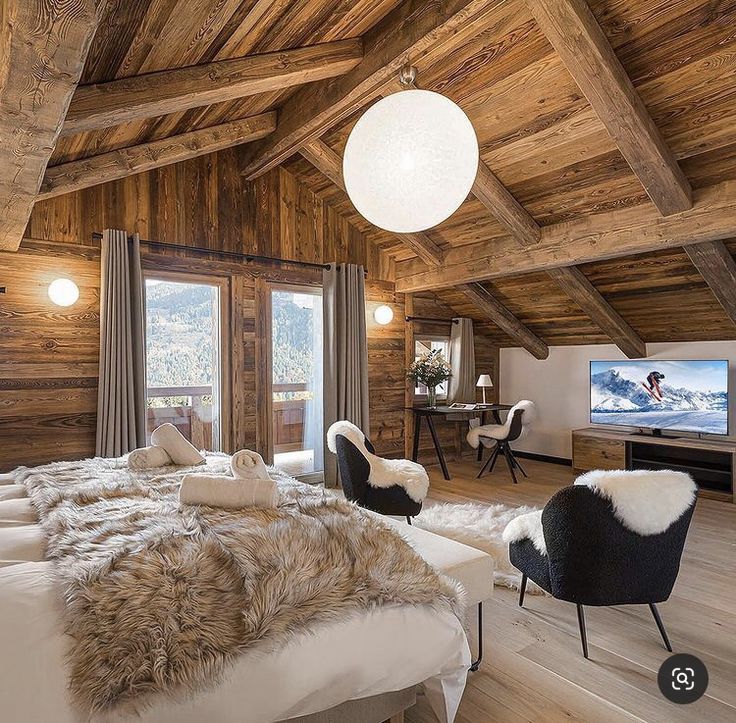 a bedroom with wood paneling and white fur on the bedspread, two black chairs in front of a flat screen tv