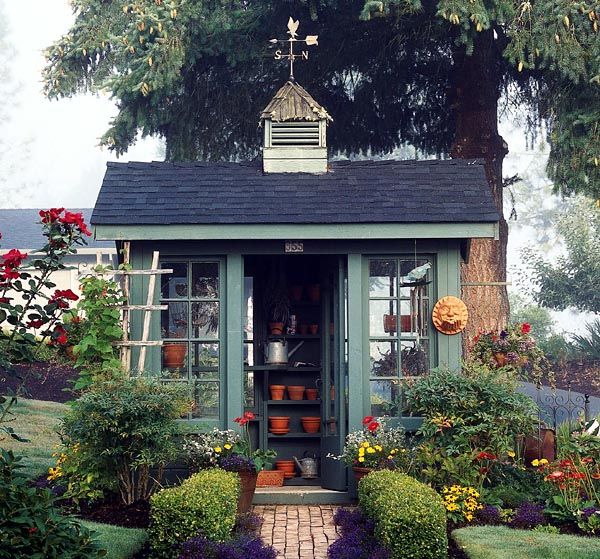 a small garden shed with lots of potted plants and flowers on the front door