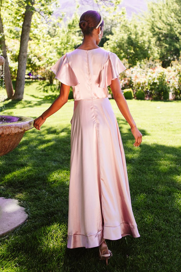 Say hello the Callie Dress in Blush Satin - a timeless choice for your bridal party ensemble! Crafted from luxurious blush pink satin fabric, this dress features a chic V-neckline and delicate half-length flutter sleeves, adding a touch of femininity to the look. The maxi-length faux wrap skirt with ruffle hem detailing exudes elegance and grace, ensuring your bridesmaids will shine all day long. Designed for both style and comfort, the Callie Dress is a stunning addition to any wedding celebrat Elegant Pink V-neck Bridesmaid Dress, Pink V-neck Satin Dress For Formal Occasions, Pink Short Sleeve Bridesmaid Dress For Party, V-neck Satin Finish Bridesmaid Dress, Feminine Satin V-neck Dress, Elegant V-neck Satin Dress For Bridesmaids, Elegant Pink V-neck Satin Dress, Elegant Pink Satin Bridesmaid Dress, Elegant V-neck Satin Bridesmaid Dress