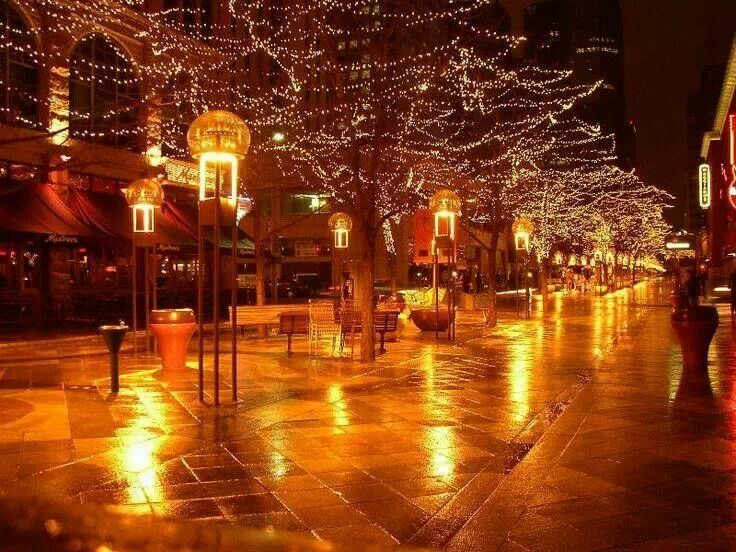 a city street at night with christmas lights on the trees and buildings in the background