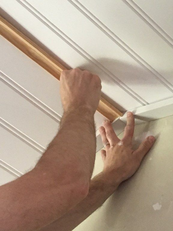 a man is working on the ceiling in his home with white paint and wood trimming