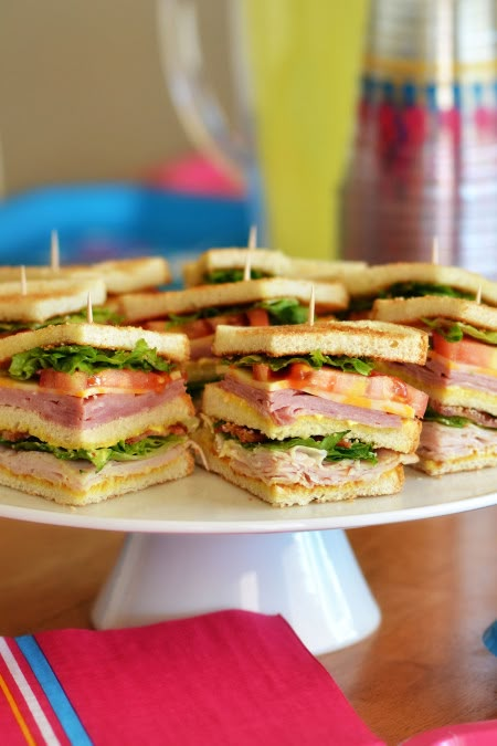 there are many sandwiches stacked on the cake plate with toothpicks stuck in them