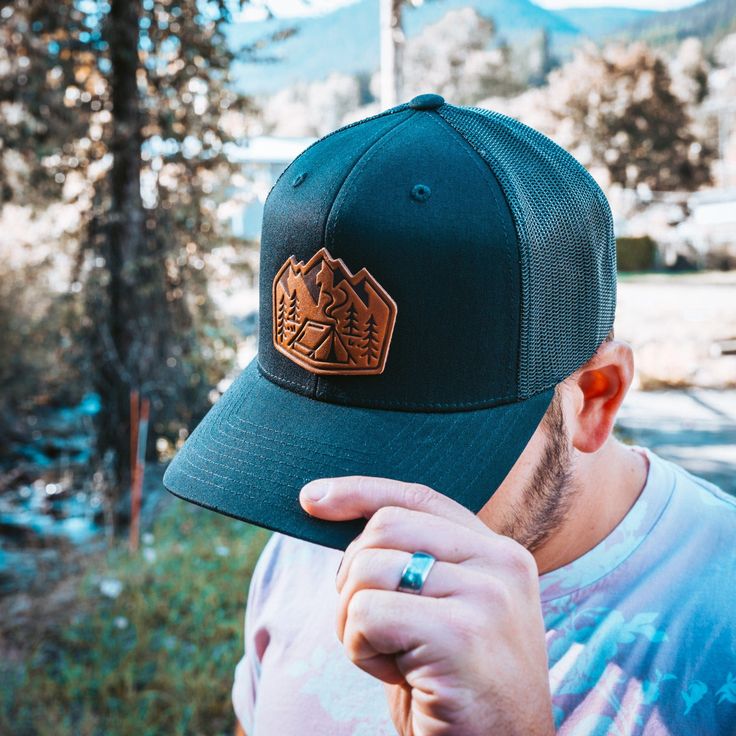 Camp. Conquer. Repeat. This isn’t your trendy, overpriced fashion accessory. It’s a reliable, no-nonsense piece of gear for people who actually enjoy the outdoors. The leather patch says it all—mountains, trees, and a tent. It’s simple, just like a good campfire under the stars. No need for gimmicks, just a symbol of nature at its finest. This hat wasn’t made to sit pretty on a shelf. It was made to be worn, whether you're setting up camp, chopping wood, or just sitting in a lawn chair by the fi Black Six-panel Hat For Camping, Outdoor Flat Bill Hat With Logo Patch, Flat Bill Hats With Logo Patch For Outdoor, Black Six-panel Hiking Hat, Black Six-panel Hat For Hiking, Outdoor Cap With Logo Patch, Camping Trucker Hat With Logo Patch, Snapback Baseball Cap With Logo Patch For Camping, Logo Patch Trucker Hat For Camping