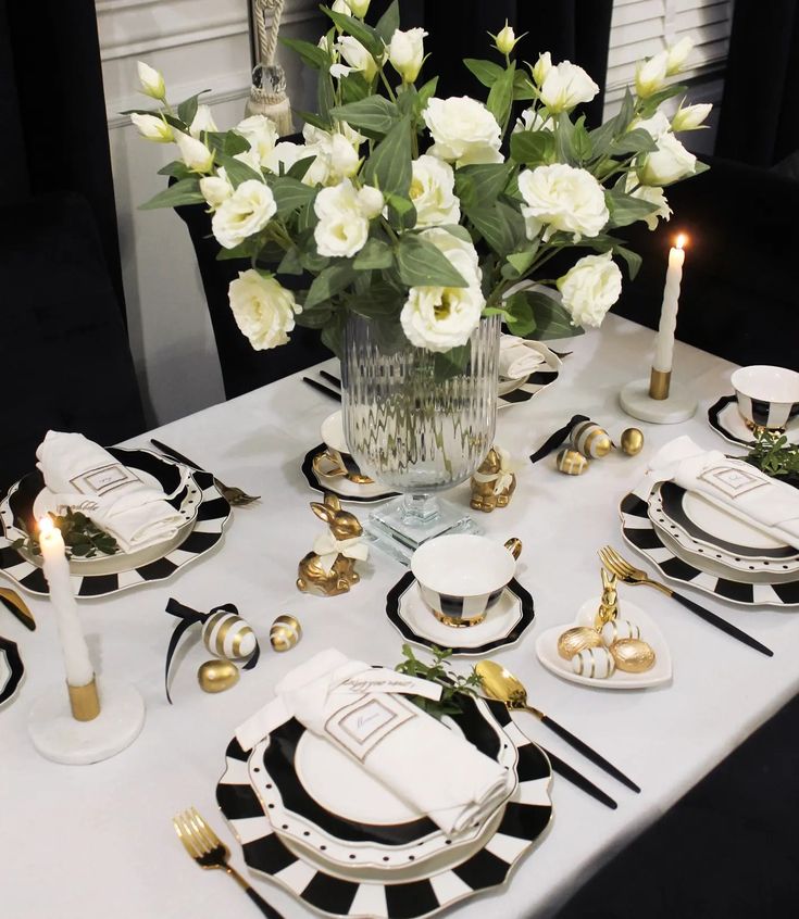 the table is set with black and white plates, silverware, and flowers in a vase