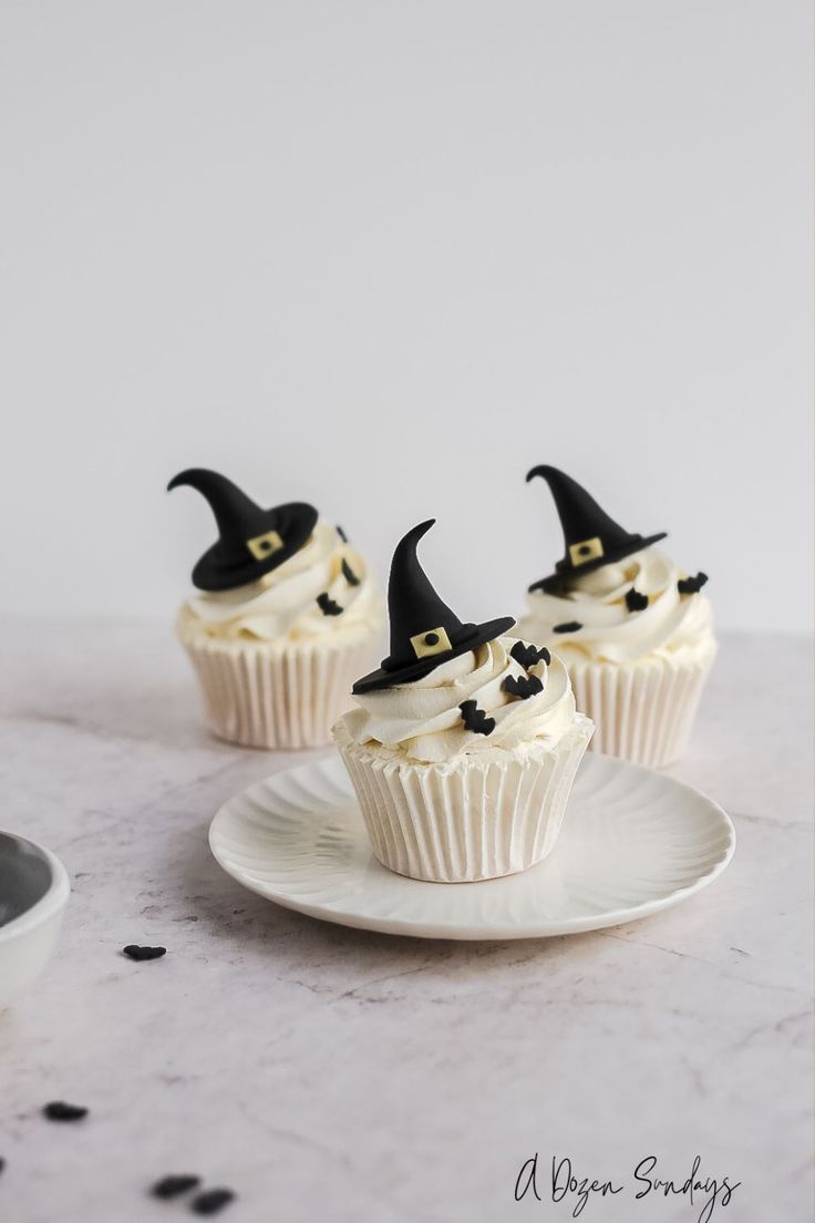 three cupcakes with white frosting and black witches hats on them sitting on a plate