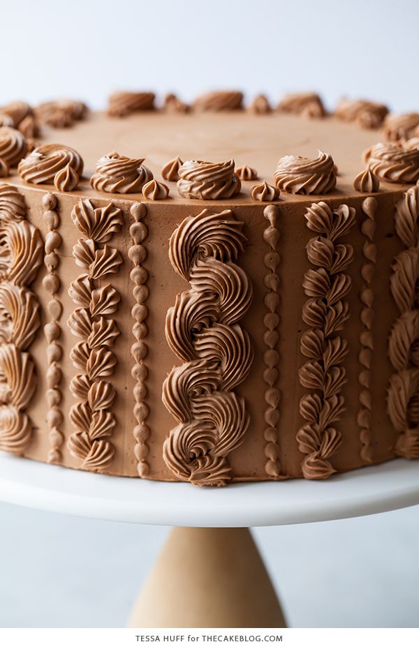 a chocolate cake sitting on top of a white cake plate with frosting swirls