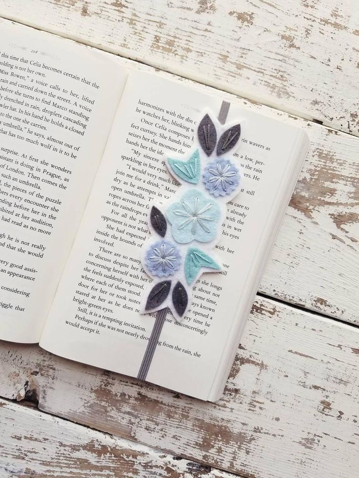 an open book with paper flowers on it sitting on top of a white wooden table