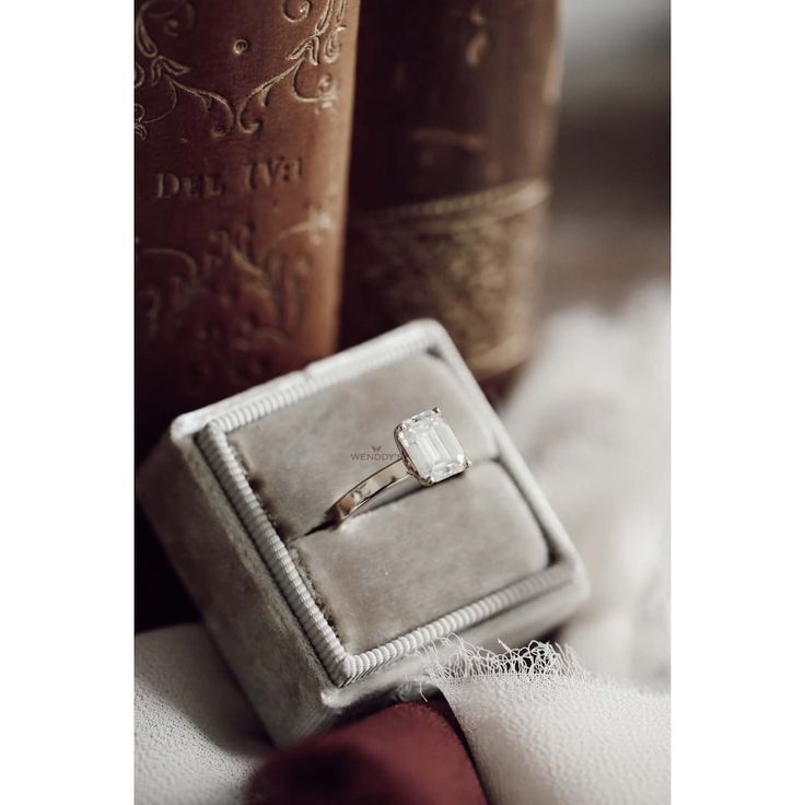 an engagement ring sitting on top of a box next to two book's in the background