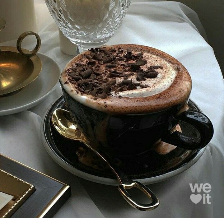 a cup of hot chocolate with whipped cream on top sitting on a saucer next to a glass vase