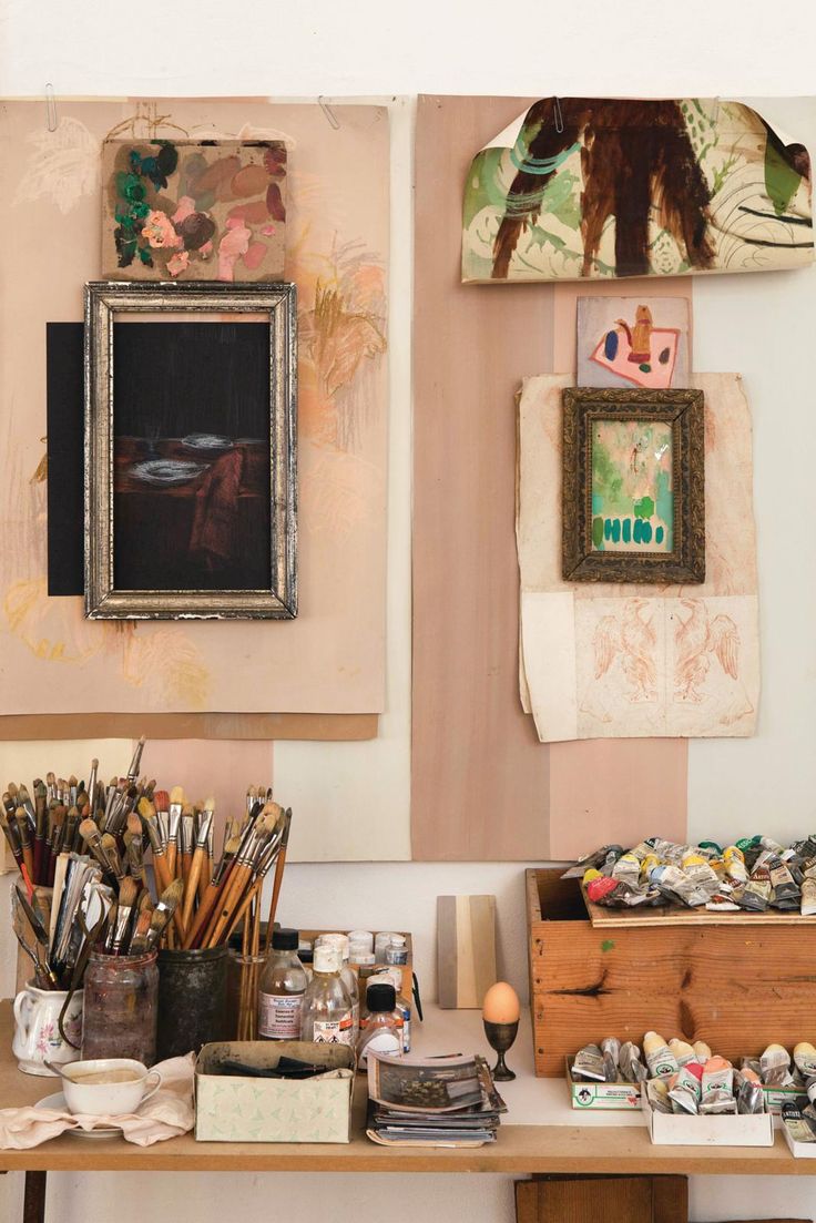 an artist's desk with art supplies and paintings on the wall