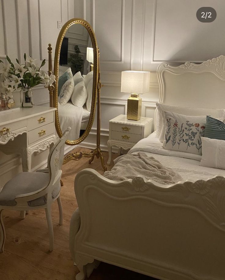 a white bed sitting in a bedroom next to a table with a mirror on it