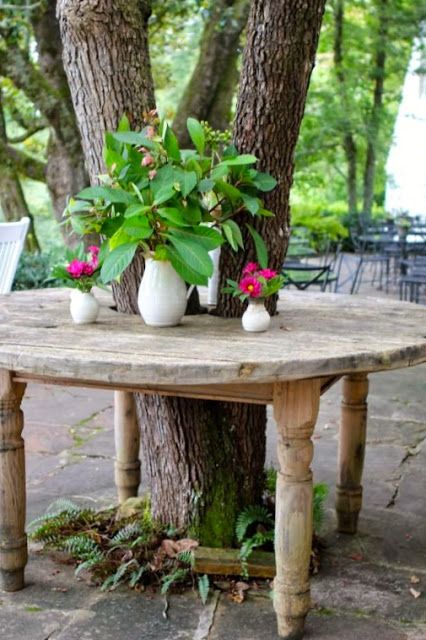 a table with potted plants on it in the middle of a patio area next to a tree