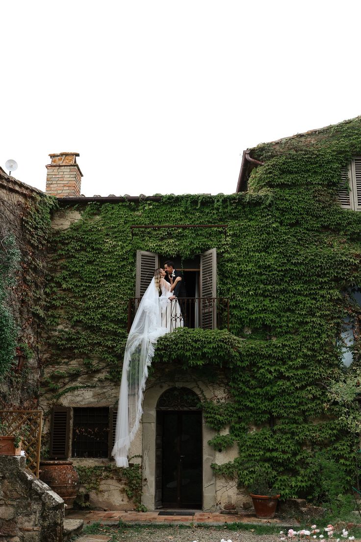 a bride and groom standing on the balcony of an old building with ivy growing all over it