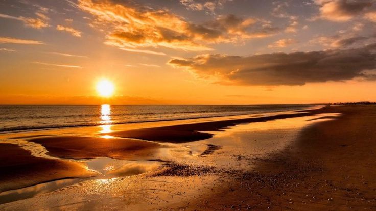 the sun is setting over the water at the beach with waves coming in to shore