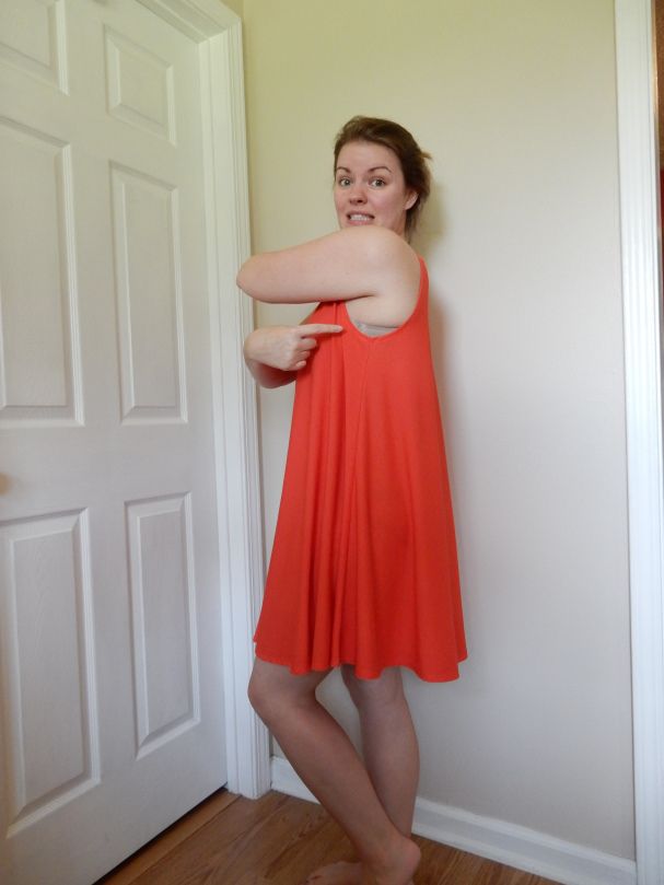 a woman in an orange dress leaning against a wall with her arms behind her back